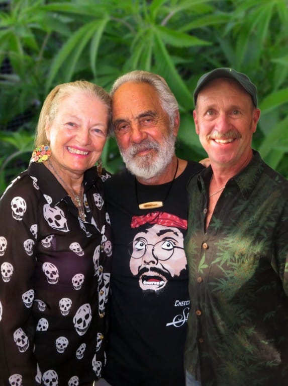 Three individuals stand together in front of a large marijuana plant, posing for a presentation cover image.